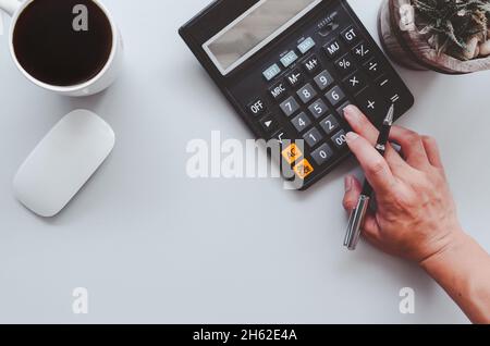 Uomo tenendo una penna e premendo una calcolatrice.Vista superiore e spazio di copia sullo sfondo.mouse computer e caffè tazza. Foto Stock