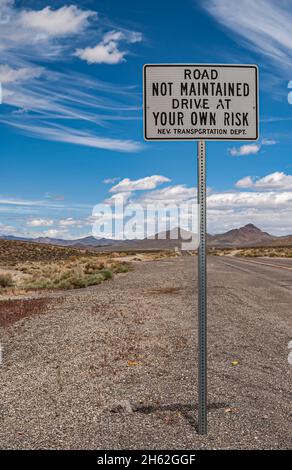 Tonopah, Nevada, Stati Uniti - 16 maggio 2011: Primo piano del cartello stradale avvertimento strada non è mantenuto, guidare a proprio rischio contro il paesaggio blu. Montagna grigia Foto Stock