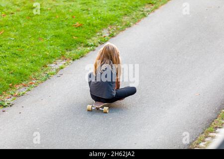 la ragazza si siede sul suo skateboard e corre su una strada da gioco Foto Stock