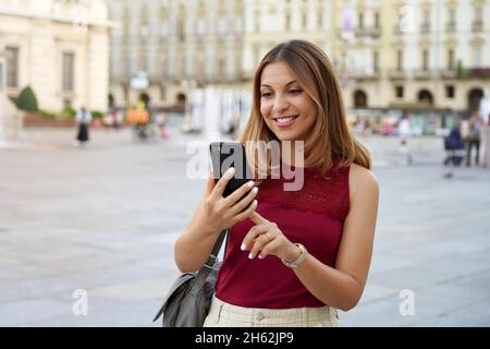 Attraente giovane donna multietnica che utilizza un dispositivo per videochiamate o social network con sfondo urbano sfocato Foto Stock