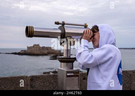 francia,bretagna,ille et vilaine,saint malo,ragazzo guarda attraverso un telescopio, isola marea petit-bé con il forte nazionale, costa atlantica Foto Stock