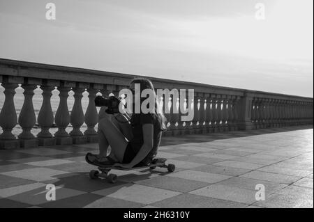 skater ragazza pattinare e saltare sulla terrazza mascagni a livorno, italia. il suo ampio belvedere sinuoso verso il mare con una superficie di pavimentazione di 8700 mq come una scacchiera e 4,100 balaustre Foto Stock