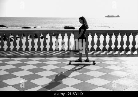 skater ragazza pattinare e saltare sulla terrazza mascagni a livorno, italia. il suo ampio belvedere sinuoso verso il mare con una superficie di pavimentazione di 8700 mq come una scacchiera e 4,100 balaustre Foto Stock