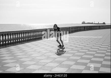 skater ragazza pattinare e saltare sulla terrazza mascagni a livorno, italia. il suo ampio belvedere sinuoso verso il mare con una superficie di pavimentazione di 8700 mq come una scacchiera e 4,100 balaustre Foto Stock
