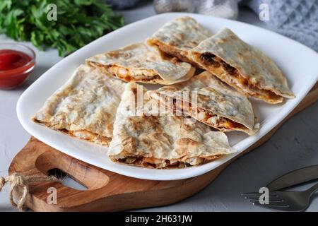 Spuntino messicano quesadilla da tortilla con pollo, formaggio e champignon in piatto bianco su tavola di legno Foto Stock