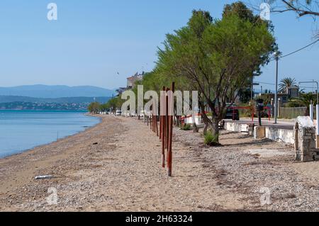 in grecia c'è una spiaggia di sabbia, alcuni pioli arrugginiti che escono dalla sabbia e si godono la vista sull'oceano e sulle montagne sul retro. anche gli alberi sono nella foto. Foto Stock