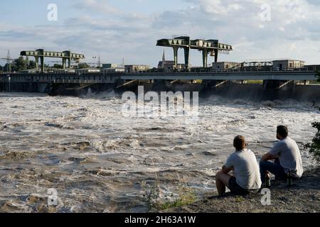 germania,baviera,alta baviera,neuötting,inn,inn centrale elettrica inn,alluvione,acqua nuvolosa,flusso veloce,due giovani uomini siedono sulla banca e guardano Foto Stock