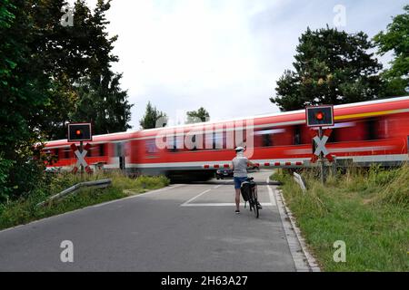 germania,baviera,alta baviera,neuötting,strada di campagna,attraversamento a livello limitato,ciclisti in attesa,treno locale che passa attraverso Foto Stock