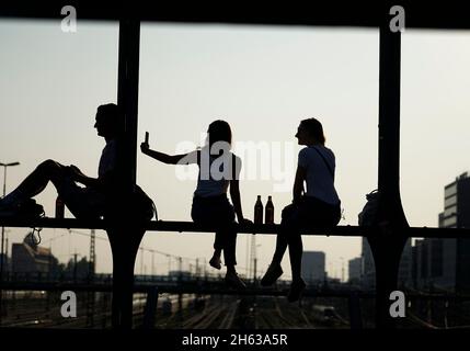 germania,baviera,monaco,stazione centrale,haccurbrücke,giovani seduti sulla struttura in ferro,freddo,in attesa del tramonto,silhouette Foto Stock