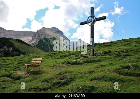 plumsjoch (1650m) sullo sfondo il vorgipfel e le bettlerkarspitze (2268 m) a destra di esso la schaufelspitze e la cresta di discesa, nel eng in montagna karwendel, rissbachtal, tirolo, austria, europa, alm, in primo piano una panchina con un cappello dietro la croce di montagna in direzione jogerch alm Foto Stock