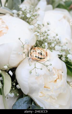 primo piano bouquet nuziale in bianco con peonie e gypsophila, anelli di nozze e anello di fidanzamento a fuoco Foto Stock