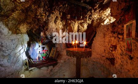 grecia,isole greche,isole ionie,cefalonia,vicino argostoli,lassi,chiesa grotta di agios gerasimos,grotta eremita,candelieri con candele brucianti,icone poco illuminate di fronte alla parete rocciosa Foto Stock