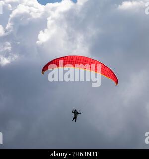 pilota di parapendio con ombrello rosso davanti alle nuvole, sopra sillian in hochpustertal, tirolo orientale, distretto di lienz, tirolo, austria Foto Stock