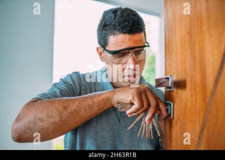 Fabbro che apre una porta. Primo piano della riparazione a mani maschili o installazione di una serratura metallica della porta con un cacciavite. Migliore protezione contro le rapine. Dispositivo di bloccaggio. Foto Stock