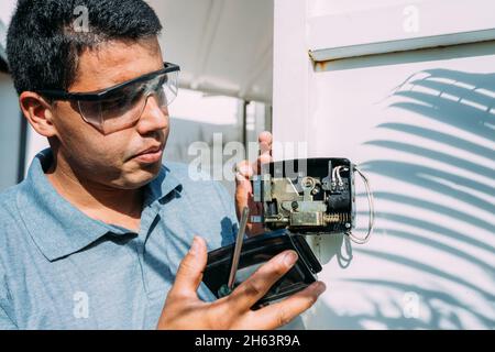 Primo piano della riparazione a mani maschili o dell'installazione di una serratura elettronica in metallo della portiera. Foto Stock