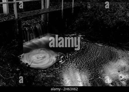 lunga esposizione di un piccolo fiume ad uno stramazzo nella foresta in autunno, bianco e nero Foto Stock