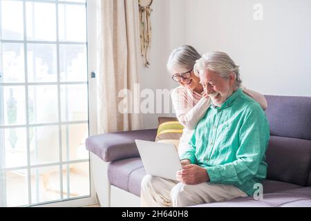 due persone anziane e mature a casa usano il tablet in un divano. i senior usano il notebook divertendosi e divertendosi a guardarlo. concetto di tempo libero e libero Foto Stock