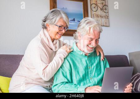 due persone anziane e mature a casa usano il tablet in un divano. i senior usano il notebook divertendosi e divertendosi a guardarlo. concetto di tempo libero e libero Foto Stock