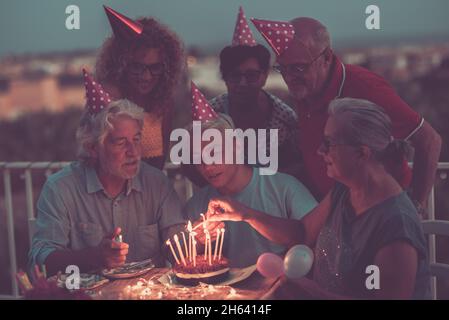 festa di compleanno della famiglia di notte con torta e candele di fuoco - famiglia con i padri e nonni ragazzo godere e divertirsi tutti insieme sorridendo e divertirsi Foto Stock