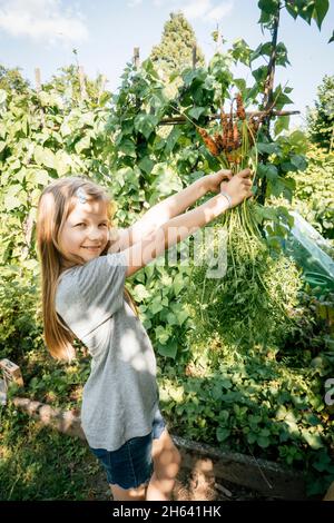 ragazza che tiene un mazzo di carote appena raccolte nel giardino Foto Stock