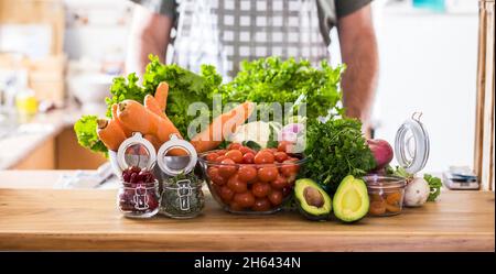 verdure fresche con peperoncini secchi ed erbe sul banco della cucina mentre lo chef in grembiule è pronto a preparare la cena. frutta biologica, verdure e spezie sane sul piano della cucina. Foto Stock