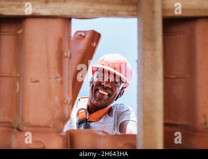 Operatore latino che installa tegole gialle in ceramica montate su tavole di legno che coprono il tetto di edifici residenziali in costruzione. Foto Stock