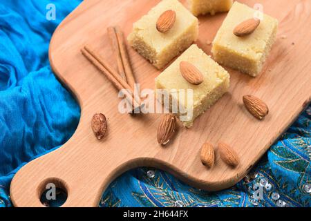 Halava, dolci indiani tagliati in piazze decorate con mandorle su tavola di legno su tela indaco vista dall'alto Foto Stock