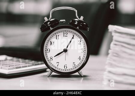 sveglia orologio sul tavolo da lavoro dell'ufficio per le ore di lavoro in bianco e nero Foto Stock