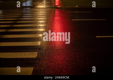 Il colore rosso del semaforo si riflette sul passaggio pedonale. Luce rossa sull'autostrada. Foto Stock