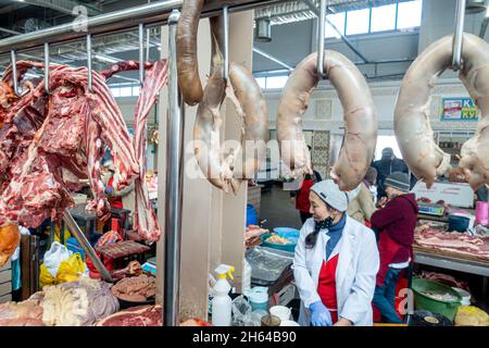 Una donna kazaka al banco che vende carne di cavallo appesa, qazy, salsiccia di cavallo. Mercato della carne ad Altyn Orda, Almaty, Kazakhstan Foto Stock