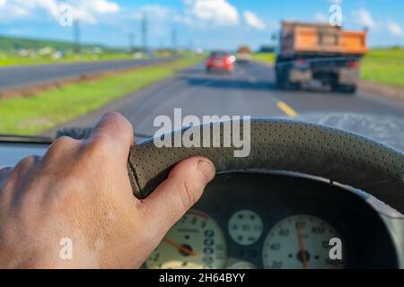 vista della mano del conducente sul volante della vettura tra il flusso di altri trasporti Foto Stock