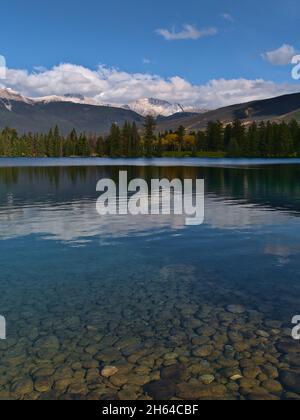 Splendida vista panoramica del bellissimo lago Beauvert di Jasper, Alberta, Canada, sulle Montagne Rocciose con pietre rotonde illuminate sulla riva. Foto Stock