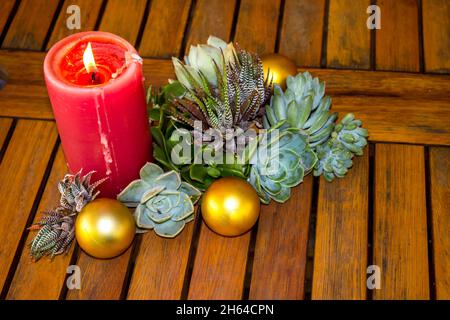 Un Natale ancora-vita costituito da una candela illuminata, varie succulenti e palle d'oro, su un rustico tavolo di legno. Foto Stock