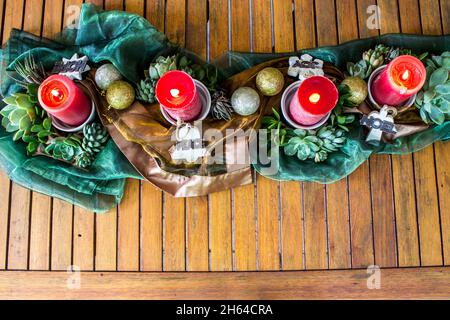 Una decorazione del tavolo di Natale sudafricano consiste di quattro candele rosse illuminate circondate da tessuto verde lucido e di bronzo e varie piante succulente Foto Stock