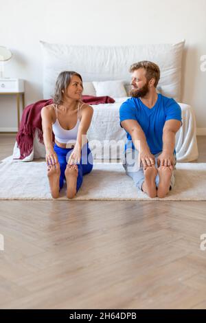 Una coppia di mezza età che si allunga insieme a casa. Si guardano e sorridono. Foto Stock