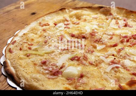 Crostate Flambe o Flammkuchen su tagliere di legno, torta tradizionale alsaziana con formaggio, cipolla e prosciutto Foto Stock