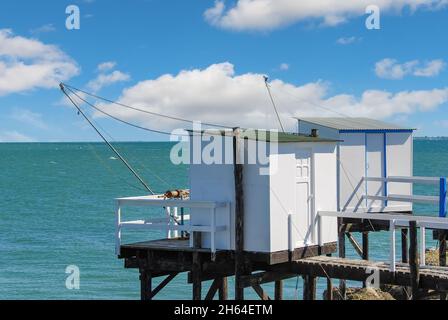 Vista delle tradizionali capanne da pesca su palafitte con carrelets sospesi (reti da pesca) lungo l'estuario della Gironda vicino Boardeax, Francia con Oceano Atlantico Foto Stock