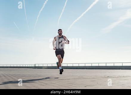 Fit giovane che corre lungo il lungomare. Corridore maschio che fa jogging la mattina presto. Atleta che pratica allenamento fitness all'aperto. Allenamento durante il blocco outsi Foto Stock
