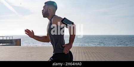 Fit giovane che corre lungo il lungomare. Corridore maschio che fa jogging la mattina presto. Atleta che pratica allenamento fitness all'aperto. Allenamento durante il blocco outsi Foto Stock