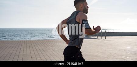 Fit giovane che corre lungo il lungomare. Corridore maschio che fa jogging la mattina presto. Atleta che pratica allenamento fitness all'aperto. Allenamento durante il blocco outsi Foto Stock