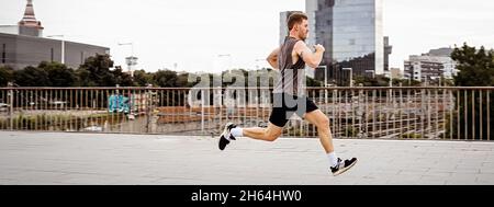 Montare l'uomo giovane che corre. Corridore maschio che fa jogging la mattina presto. Atleta che pratica allenamento fitness all'aperto. Allenati durante il periodo di chiusura fuori dalla palestra. Foto Stock
