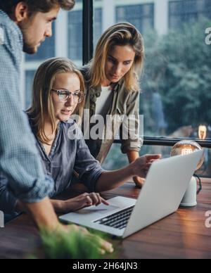 Gruppo di giovani colleghi che utilizzano un notebook. Persone che lavorano o studiano insieme. Team aziendale in ufficio. Lavoro di squadra. Concetto di avvio Foto Stock