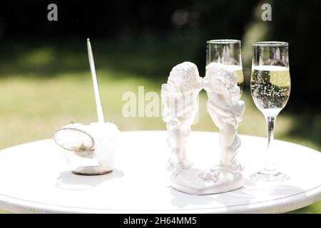 Angeli di porcellana bianca di un ragazzo e di una ragazza baciando sullo sfondo del verde sul tavolo con vetri per gli sposi novelli Foto Stock