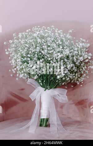 bouquet nuziale di fiori con nastro bianco si erge su una sedia rosa Foto Stock