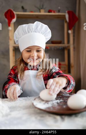 Bambina panettiere. Il bambino prepara il pan di zenzero o il biscotto di Natale e prende le uova dal piatto. Ritratto dello chef del bambino con cotto fatto in casa Foto Stock