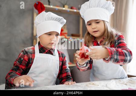 Panettieri ragazzo e ragazza che tagliano i biscotti di Natale con una muffa, facendo l'albero di Natale del pan di zenzero sul tavolo, i bambini che cucinano la vigilia di Natale. Foto Stock