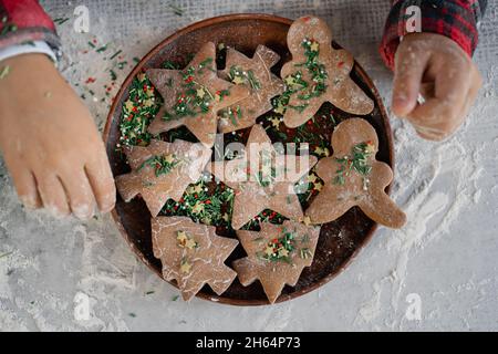 Piatto con biscotti natalizi di pan di zenzero sul tavolo. Mani dei bambini con un piatto di biscotti a forma di stella, uomo e spina di pesce. Foto Stock