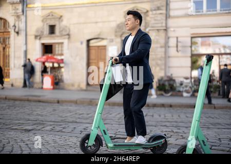 Uomo d'affari asiatico che guida scooter elettrico in città Foto Stock