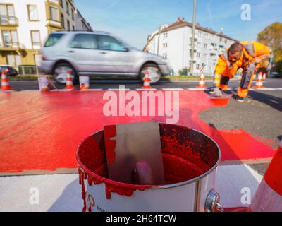 10 novembre 2021, Hessen, Francoforte sul meno: Un operaio dipinge la vernice rossa per la pista ciclabile. In Gartenstraße/Walter-Kolb-Straße un percorso ciclabile è contrassegnato con vernice rossa. Foto: Andreas Arnold/dpa Foto Stock