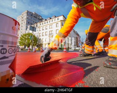 10 novembre 2021, Hessen, Francoforte sul meno: Un operaio dipinge la vernice rossa per la pista ciclabile. In Gartenstraße/Walter-Kolb-Straße un percorso ciclabile è contrassegnato con vernice rossa. Foto: Andreas Arnold/dpa Foto Stock